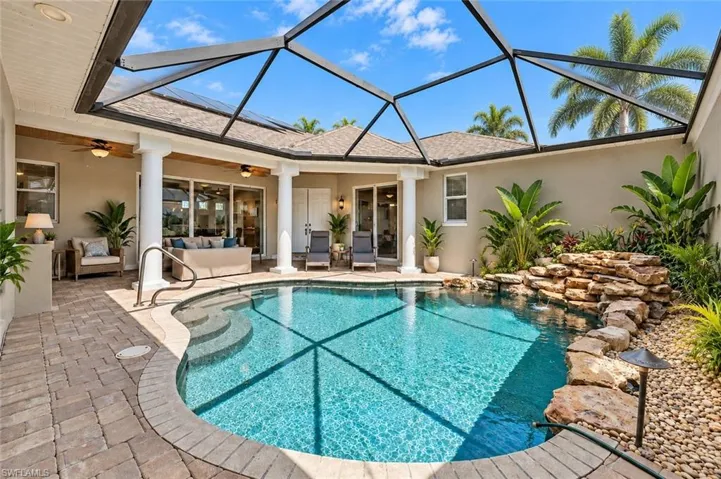 Screened-in outdoor living space with a curved pool and rock water feature. Edied with AI