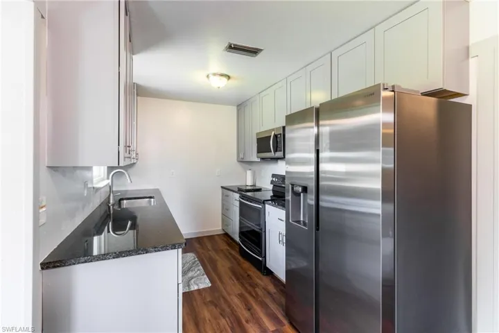 Kitchen featuring white cabinetry, stainless steel appliances, dark hardwood / wood-style flooring, sink, and dark stone countertops