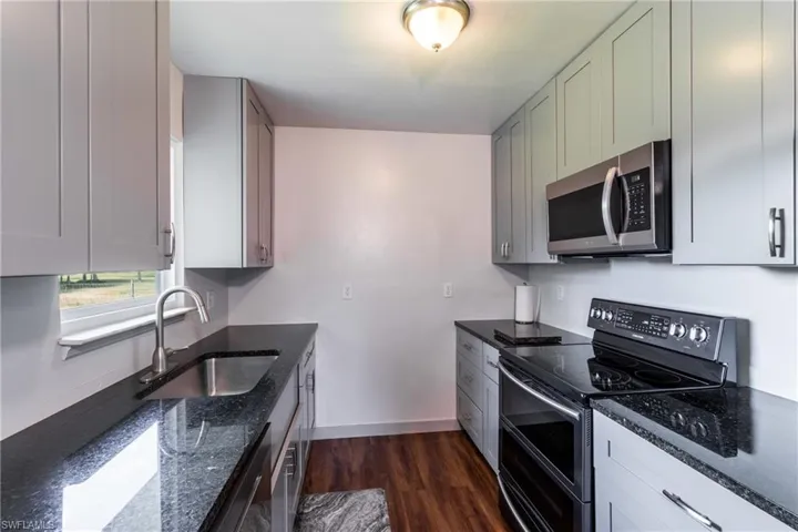 Kitchen featuring sink, appliances with stainless steel finishes, dark stone counters, and dark hardwood / wood-style flooring