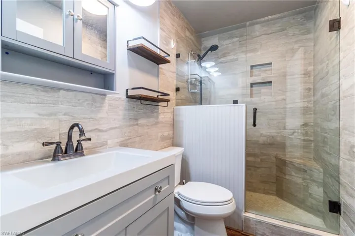 Bathroom featuring a shower with shower door, vanity, toilet, and tile walls