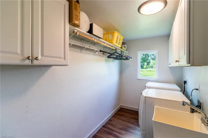 Laundry area with cabinets, washing machine and dryer, dark hardwood / wood-style flooring, and sink