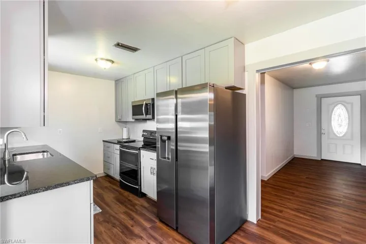 Kitchen featuring appliances with stainless steel finishes, dark stone counters, sink, dark hardwood / wood-style floors, and white cabinetry