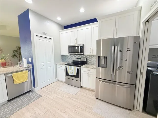 Kitchen with stainless steel appliances, backsplash, white cabinets, light stone counters, and light wood-style floors