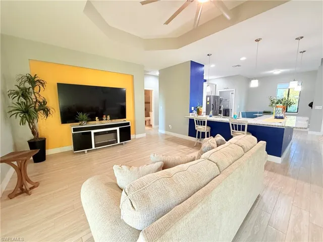 Living area with a ceiling fan, light wood-type flooring, a tray ceiling, and recessed lighting