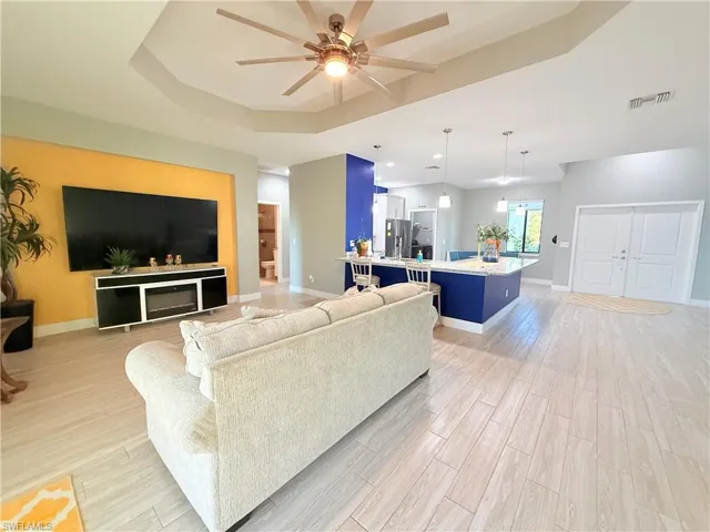Living area featuring light wood-type flooring, ceiling fan, and a raised ceiling
