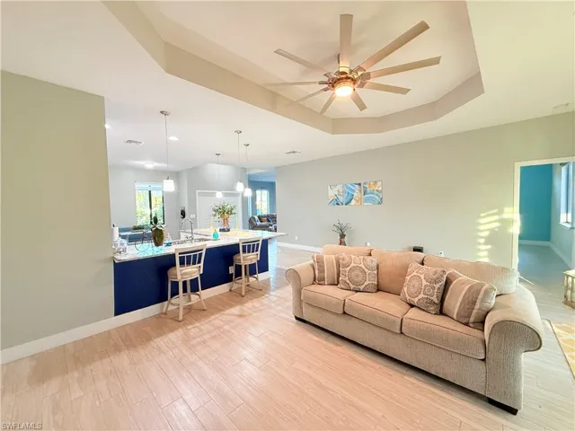 Living room with a raised ceiling, light wood-style floors, and ceiling fan