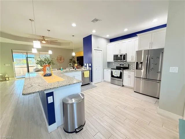 Kitchen with appliances with stainless steel finishes, light stone countertops, light wood-style floors, a peninsula, and decorative light fixtures