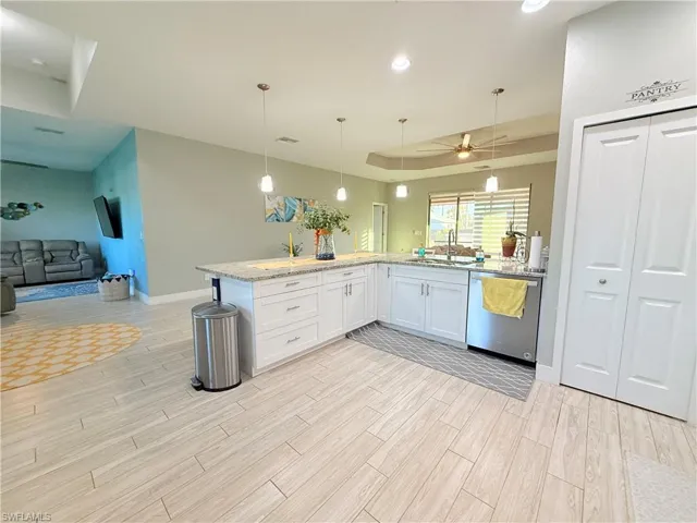 Kitchen with open floor plan, decorative light fixtures, a tray ceiling, white cabinets, and light stone counters