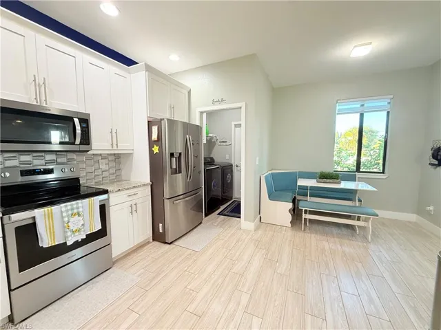 Kitchen featuring stainless steel appliances, white cabinetry, wood finish floors, backsplash, and light stone countertops