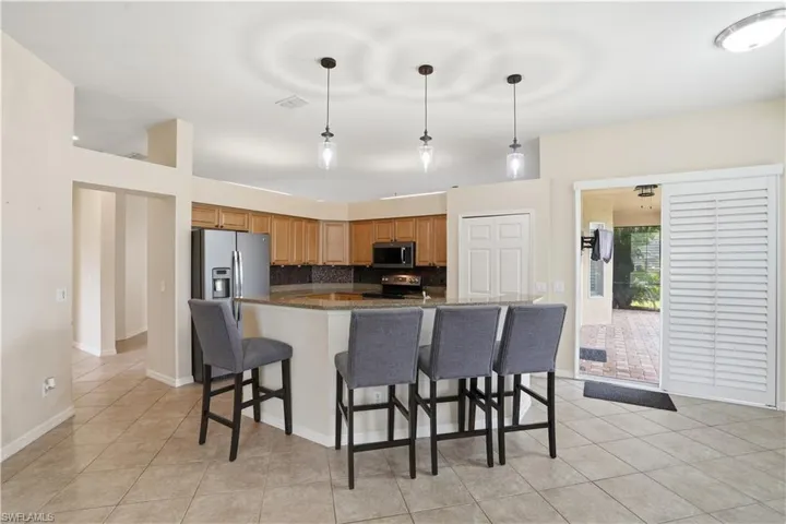 Kitchen featuring a breakfast bar with pendant lighting, wood cabinetry, stainless steel refrigerator, and a tile backsplash