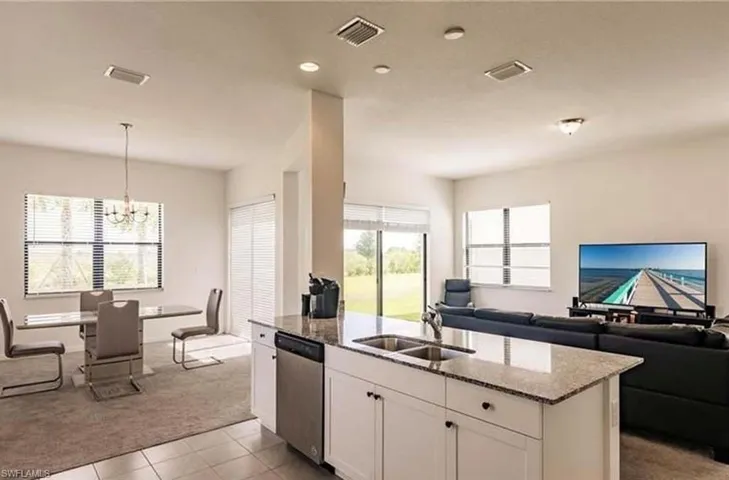 Kitchen featuring light stone counters, white cabinetry, open floor plan, light colored carpet, and a kitchen island with sink