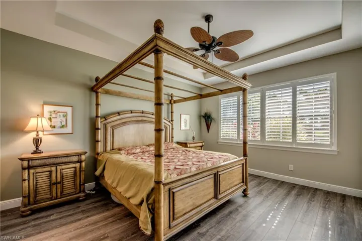 Bedroom with a raised ceiling, wood finished floors, and a ceiling fan