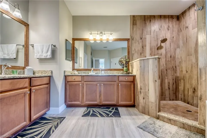 Bathroom with walk in shower, two vanities, and light wood-style flooring