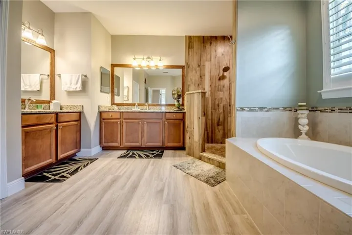 Bathroom with two vanities, a garden tub, light wood-type flooring, and a walk in shower