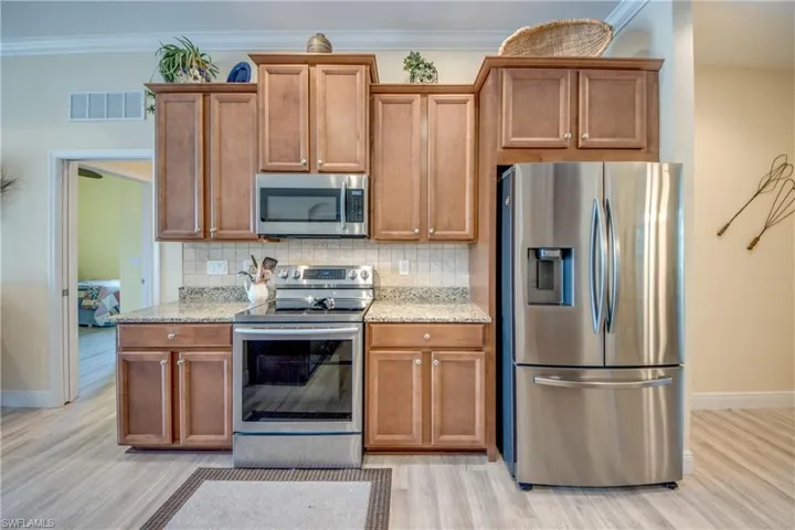 Kitchen featuring wood finish cabinetry, stainless steel appliances, light stone counters, light wood finished floors, and crown molding