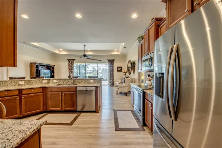 Kitchen with wood finish cabinetry, stainless steel appliances, light stone countertops, a raised ceiling, and recessed lighting