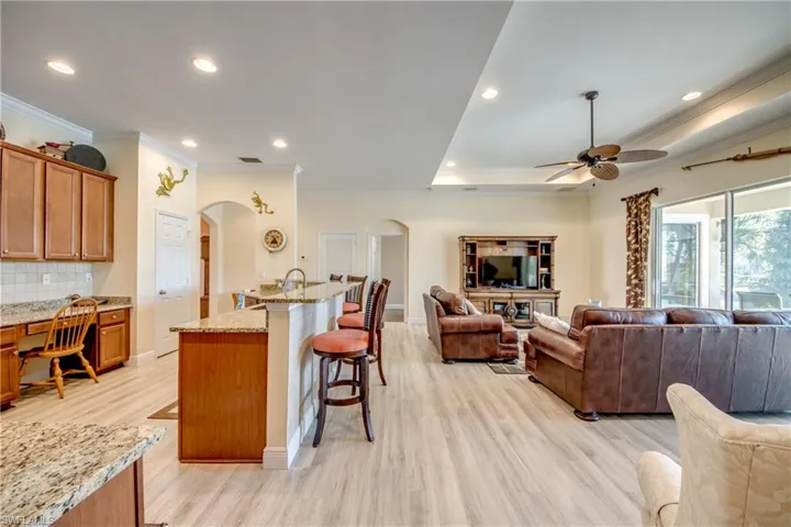 Kitchen featuring a breakfast bar, light stone countertops, wood finish cabinets, arched walkways, and light wood-style floors