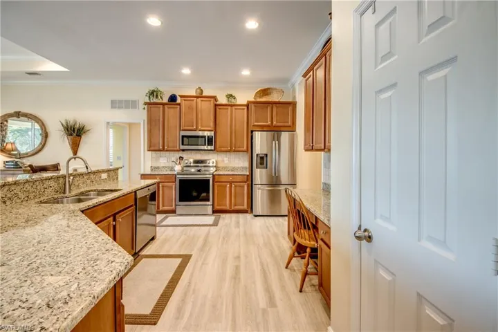 Kitchen featuring stainless steel appliances, wood finish cabinets, light stone counters, light wood-type flooring, and crown molding