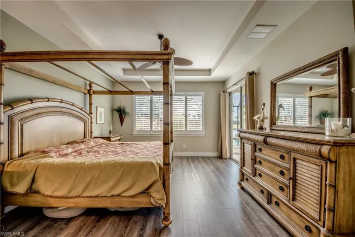 Bedroom featuring access to outside, a tray ceiling, hardwood / wood-style floors, and ceiling fan