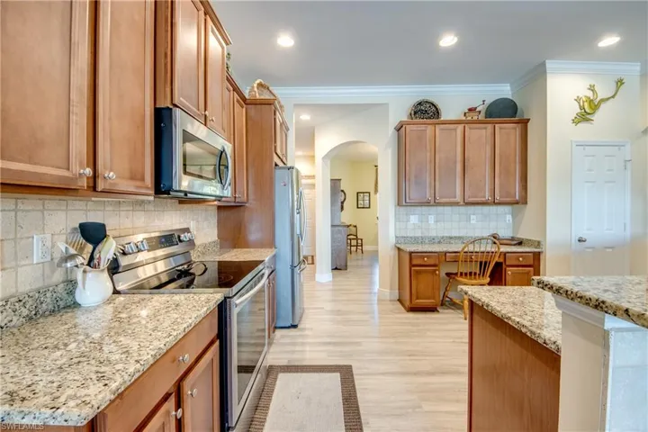 Kitchen with stainless steel appliances, decorative backsplash, arched walkways, wood finish cabinets, and light stone counters