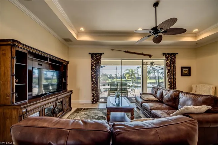 Living area featuring a tray ceiling, wood finished floors, ornamental molding, a ceiling fan, and a sunroom