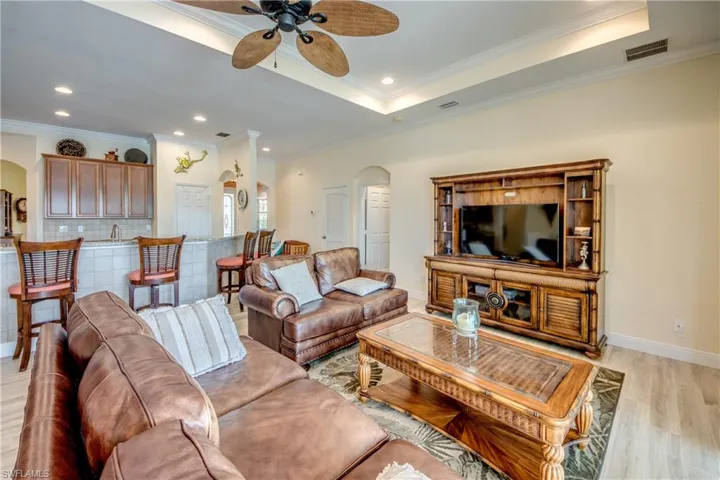 Living area with arched walkways, light wood-type flooring, a ceiling fan, ornamental molding, and recessed lighting