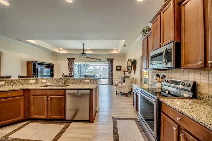 Kitchen with wood finish cabinets, stainless steel appliances, a tray ceiling, light wood finished floors, and crown molding