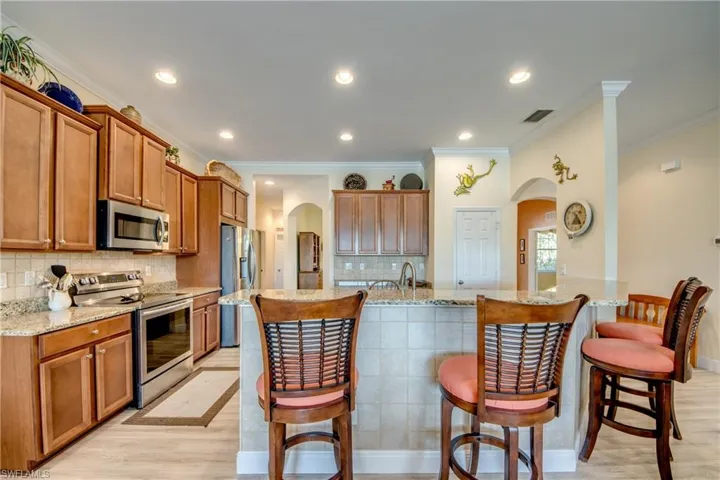 Kitchen with arched walkways, stainless steel appliances, wood finish cabinets, a breakfast bar, and light stone counters
