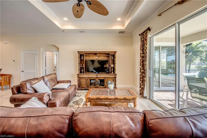 Living area with wood finished floors, arched walkways, a raised ceiling, a ceiling fan, and ornamental molding