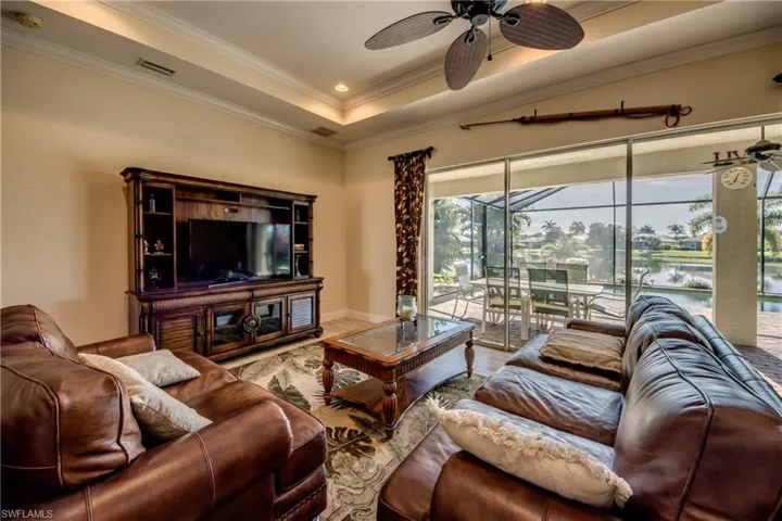 Living room with ceiling fan, a tray ceiling, crown molding, a sunroom, and wood finished floors