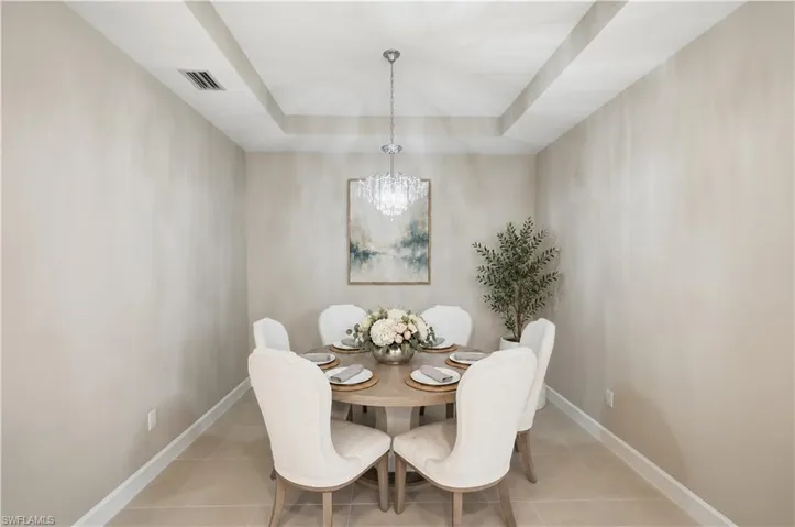 Dining area featuring a tray ceiling, crystal chandelier, and large-format tile flooring