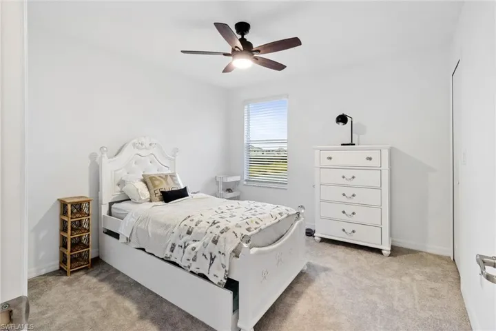 Bright bedroom featuring light-toned carpeting, a window with horizontal blinds, and a dark wood-finish ceiling fan with integrated lighting
