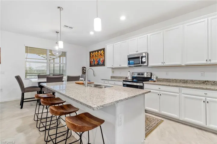Kitchen featuring an expansive island with a light-toned countertop, white cabinetry with silver hardware, stainless steel appliances, a stainless steel sink with a gooseneck faucet, and recessed lighting