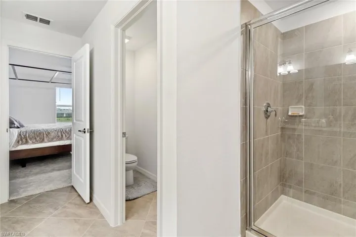 Bathroom featuring a glass-enclosed shower with tile surround, a built-in toilet, and tile flooring