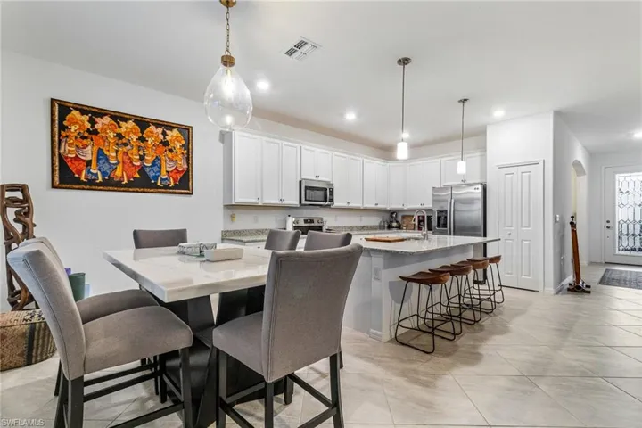 Open-concept kitchen and dining area featuring a kitchen island with seating, stainless steel appliances, white cabinetry, and light-toned tile flooring throughout