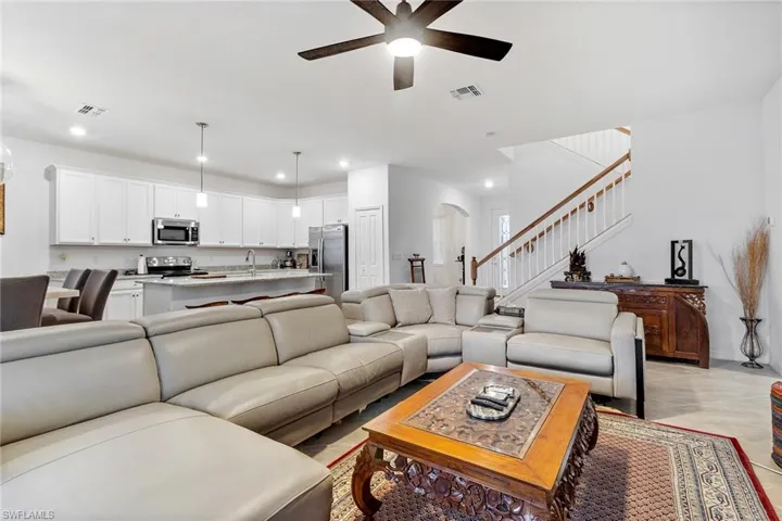 Open-concept living space featuring a kitchen with white cabinetry and stainless steel appliances, a center island with pendant lighting, and a staircase with white balusters and a wood-finish handrail