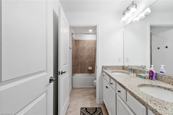 Bathroom featuring a dual-sink vanity with a granite countertop, undermount sinks, and white cabinetry