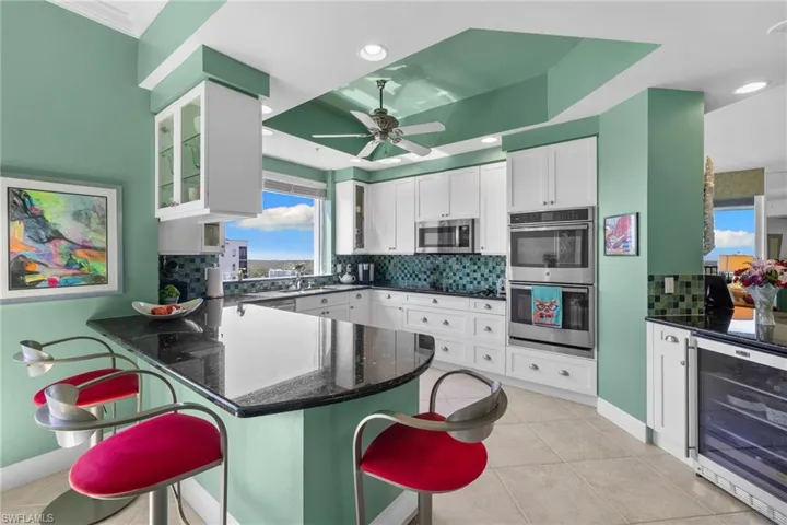 Kitchen with beverage cooler, dark stone counters, white cabinetry, backsplash, and a peninsula