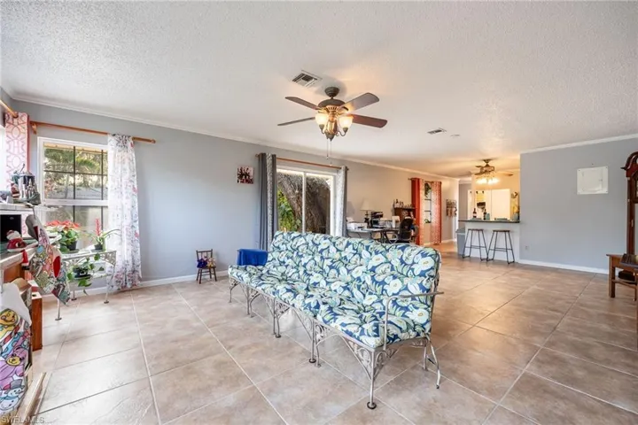 Tiled living room with crown molding, ceiling fan, and a textured ceiling