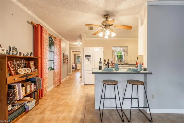 Kitchen featuring ceiling fan, light tile patterned flooring, white refrigerator with ice dispenser, and crown molding