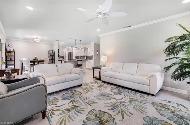 Living room with ceiling fan, light carpet, and ornamental molding