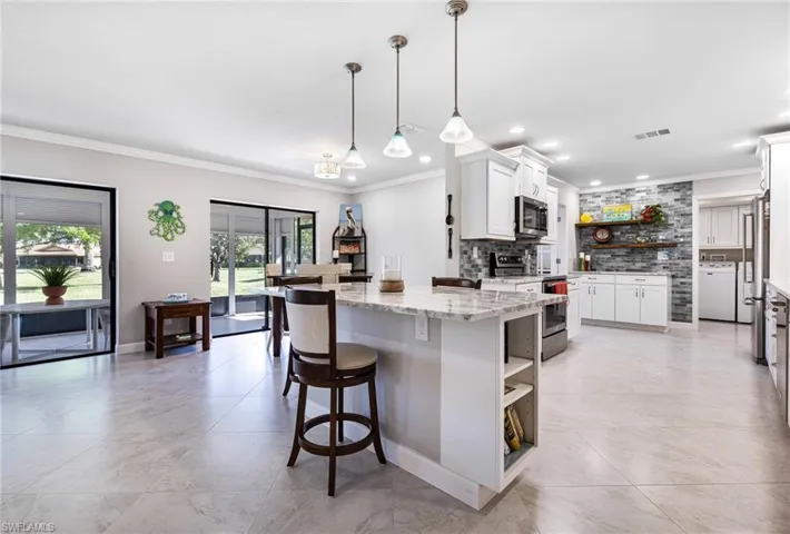 Kitchen with stainless steel appliances, pendant lighting, crown molding, light stone countertops, and white cabinetry