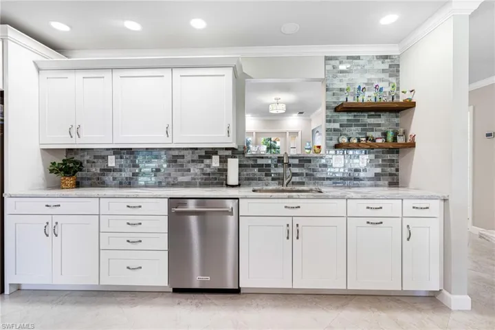 Bar with white cabinets, stainless steel dishwasher, and backsplash