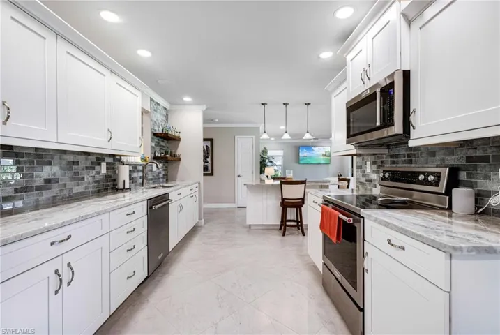 Kitchen with white cabinets, stainless steel appliances, hanging light fixtures, and crown molding