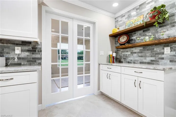 Bar with white cabinets, decorative backsplash, ornamental molding, and light stone counters