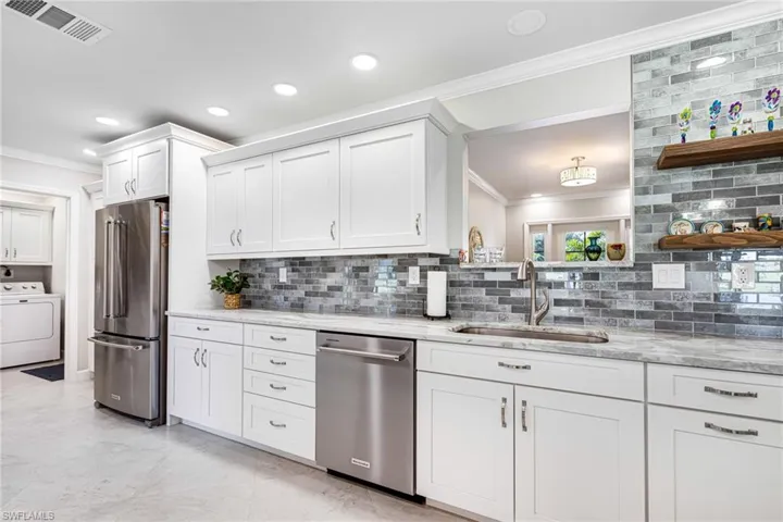 Kitchen featuring washer / dryer, appliances with stainless steel finishes, decorative backsplash, sink, and white cabinets