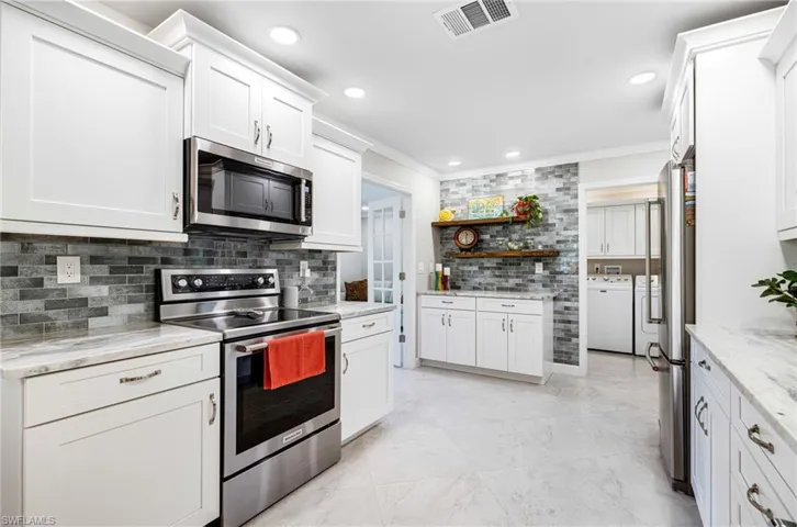 Kitchen featuring light stone counters, white cabinets, crown molding, appliances with stainless steel finishes, and independent washer and dryer