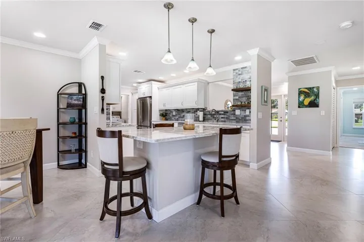 Kitchen featuring a kitchen bar, white cabinets, ornamental molding, decorative light fixtures, and stainless steel fridge
