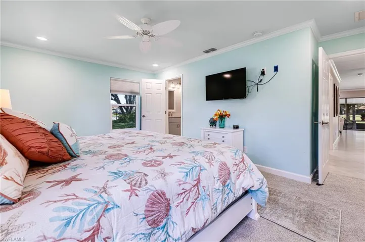 Bedroom with ensuite bath, light carpet, ceiling fan, and crown molding