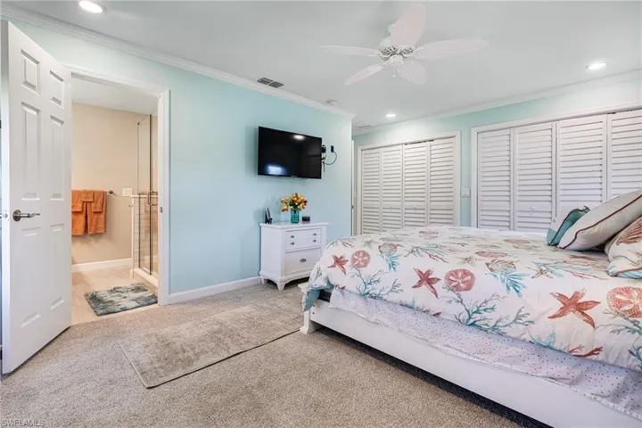 Carpeted bedroom with ornamental molding, ceiling fan, and ensuite bath